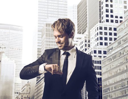 Smiling young businessman looking at his wristwatch with cityscape in the background