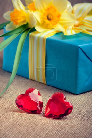 Two red glass hearts with a gift box and flowers