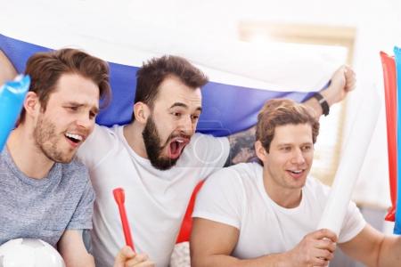 Happy male friends cheering and watching sports on tv