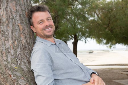 Middle aged man relaxing leaning against tree