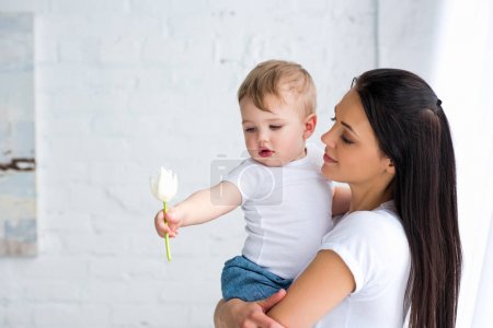 young mother holding cute baby with tulip flower in hand at home