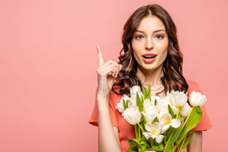 attractive girl blowing showing idea gesture while holding bouquet of white tulips isolated on pink
