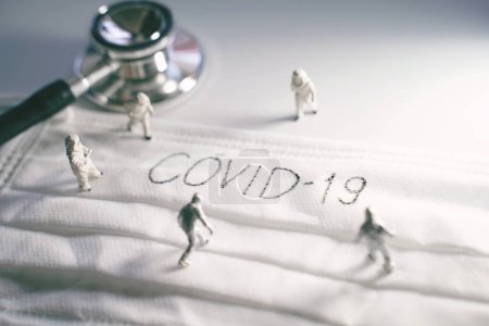 Miniature people doctors with protective suit prevention of pandemic Covid-19 and Coronavirus, surgical mask with Covid-19 text written on it with stethoscope, dramatic toned