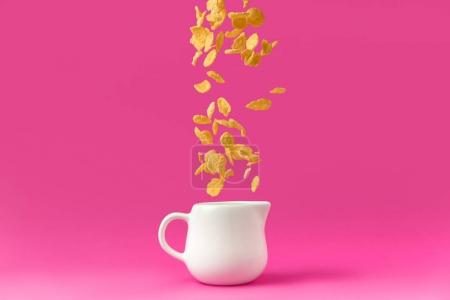 close-up view of organic corn flakes falling into milk jug isolated on pink