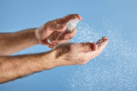 cropped view of man using hand sanitizer in spray bottle isolated on blue