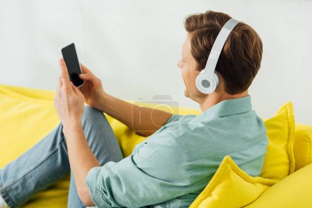 Side view of man in headphones using smartphone on couch on grey background