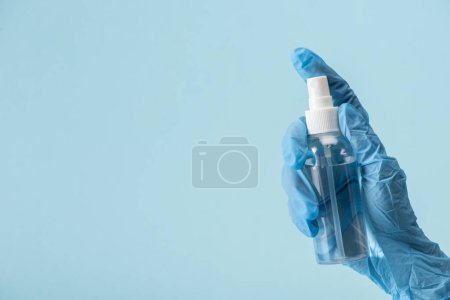 cropped view of doctor in latex glove holding bottle with hand sanitizer isolated on blue 