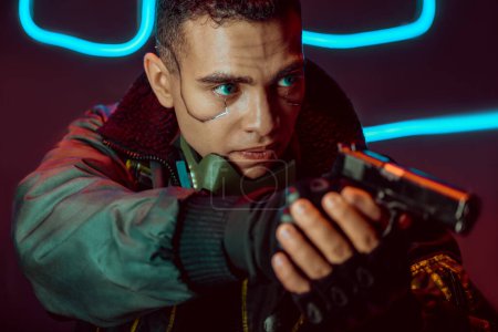 selective focus of dangerous bi-racial cyberpunk player with gun on black with neon lighting 