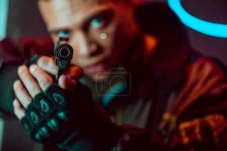selective focus of gun in hands of armed bi-racial cyberpunk player 
