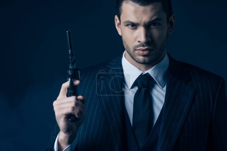 Front view of gangster holding gun and looking at camera on dark blue background