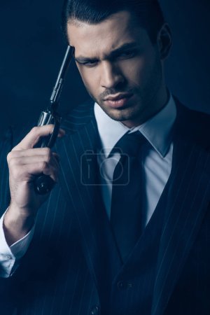 Front view of thoughtful gangster with gun on dark blue background
