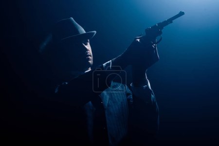 Gangster with outstretched hands aiming revolver on dark background