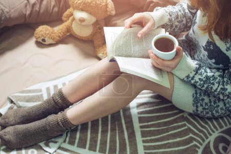 girl reading book in bed with warm socks drinking coffee
