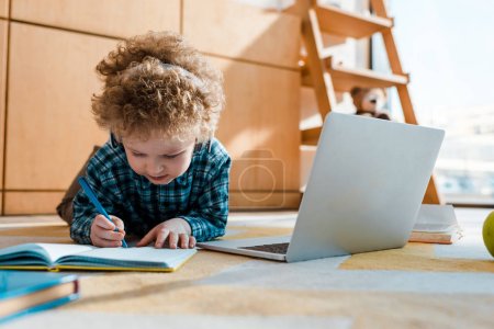 selective focus of kid listening music in wireless headphones while writing near laptop 