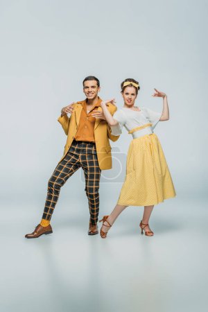 cheerful dancers looking at camera while dancing boogie-woogie on grey background