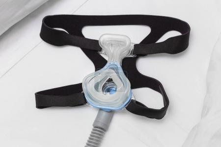 CPAP mask, headgear strap, and air hose on white bed