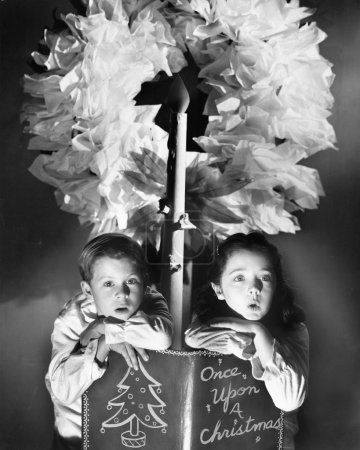 Two children sitting under a wreath holding a Christmas story book