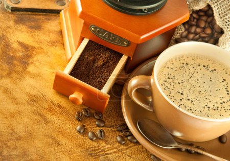 Coffee grinder in a retro style, a cup of coffee on grange background
