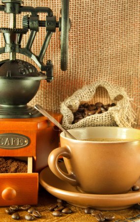 Coffee grinder in a retro style, a cup of coffee on grange background