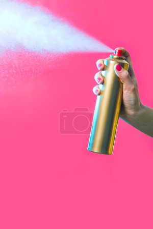 Hair lacquer in female hand spraying it over red background
