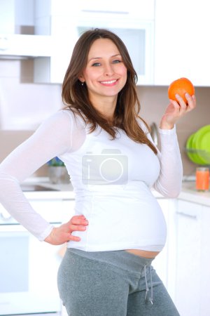 Pregnant Young Woman Eating Fruits at home kitchen