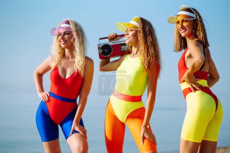 Three young woman in bright swimsuits.  Dancing on the beach.Sport, summer, fitness, urban culture concept.